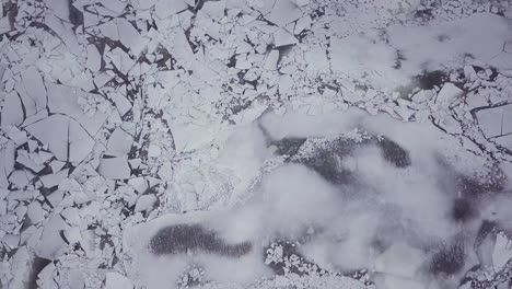 Top-down-drone-shot-flying-above-snowy-river-with-big-ice-chunks-during-a-winter-storm-in-Connecticut
