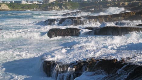 Tumultuous-ocean-waves-crashing-into-rocks,-shooting-water-straight-up-into-the-sky