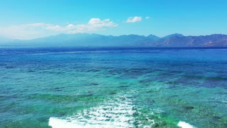 Una-Isla-En-Tonga-Paraíso-Tropical-Agua-De-Mar-Azul-Brillante-Con-Hermosa-Montaña-En-El-Fondo-Olas-Rodando-En-El-Arrecife-De-Coral