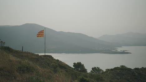 Bandera-Catalana-Ondeando-En-El-Viento-En-El-Port-De-La-Selva-Y-Vistas-A-Las-Montañas-En-La-Parte-De-Atrás