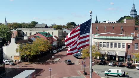 Close-up-aerial-of-US-American-flag-waving-above-Main-Street-and-State-House,-establishing-shot