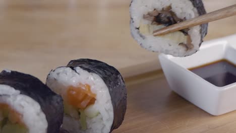 Close-Slow-Motion-Slider-Shot-of-Taking-a-Piece-of-Sushi-From-a-Wooden-Serving-Board-with-Chopsticks-and-Dipping-into-Soy-Sauce
