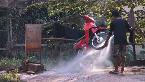 Wide-Shot-of-a-Red-Moped-Being-Cleaned-with-a-Hose-by-an-Asian-Man