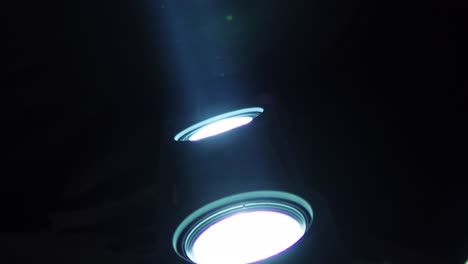 Close-up-shot-of-two-white-LED-spotlights-shining-light-upwards-with-dust-particles-flying-through-the-light-beam,-with-copy-space