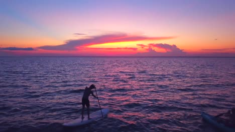 A-dramatic-drone-shot-of-a-kayaker-and-padlle-boarder-slowly-driffting-into-a-colorful-sunset
