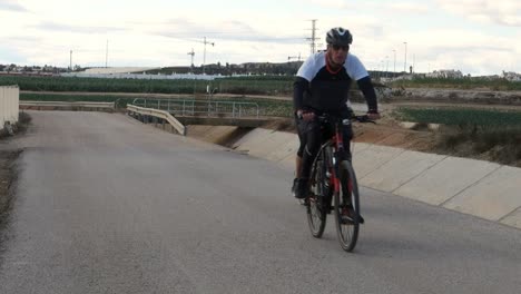 Cyclist-taking-daily-exercise-along-road-running-next-to-aqueduct-in-Spain,-slow-motion