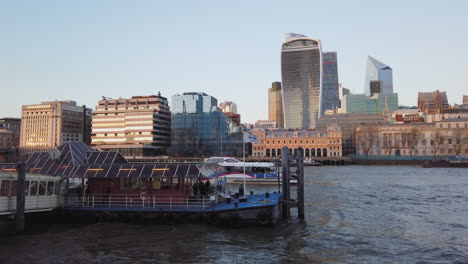 Calm-view-of-busy-Transport-for-London-pier-with-boat-and-business-building-skyline