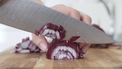 Close-side-view-as-chopping-up,-cutting-red-onion-in-the-kitchen