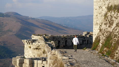 Tourist,-Der-Auf-Der-Burgmauer-Des-Krak-Des-Chevaliers-Spaziert,-Mit-Blick-Auf-Die-Weite-Syrische-Landschaft