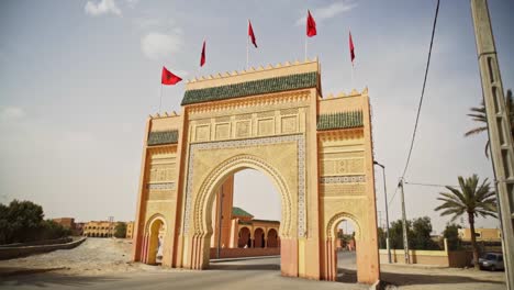 Traditional-Moroccan-gate-with-red-flags-on-top,-Gate-to-the-Sahara-Desert,-slow