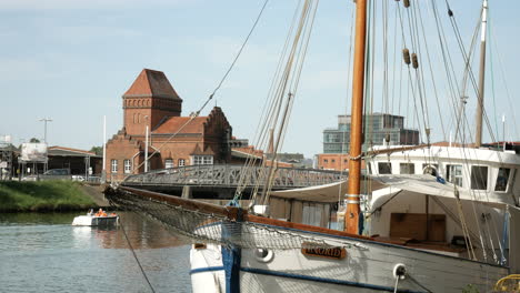 Static-shot-of-Trave-river-with-old-ship-and-modern-eco-friendly-boat-cruising-under-bridge,Lübeck-Germany