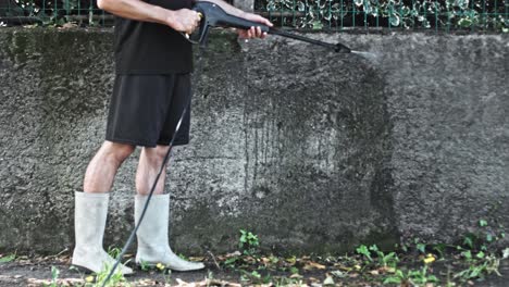 Man-using-electric-powered-pressure-washer-to-power-wash-dirty-concrete-wall