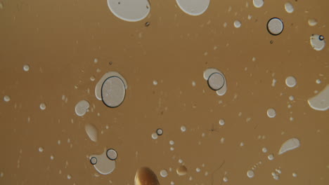 Macro-shot-of-small-bubbles-moving-in-a-golden-transparent-liquid