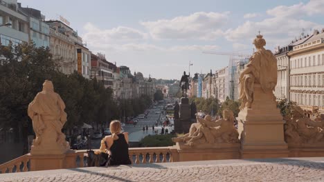 Girl-sitting-in-front-of-National-Museum-in-Prague-with-Wenceslas-square-in-background,-czech-republic