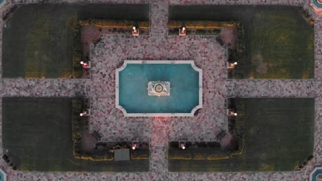 Symmetric-Birds-Eye-Aerial-View-of-Garden-With-Paved-Pathways-Revealed-From-Center-Fountain