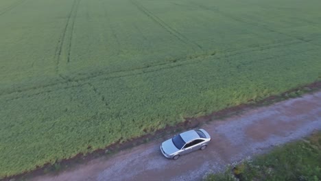 The-Car-Drives-Through-A-Gravel-Road-Towards-A-Wind-Turbine-In-Agricultural-Fields