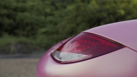 Sky-reflected-in-red-tail-light-of-pink-coated-Porsche-Boxster-two-seater-sports-car