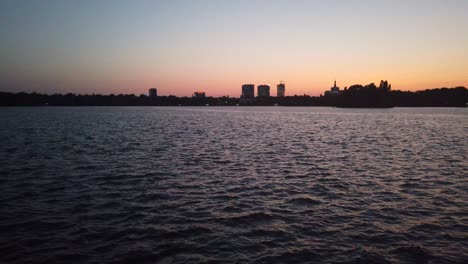 Waves-on-Herastrau-Lake,-Bucharest-at-sunset-with-distant-buildings-on-background