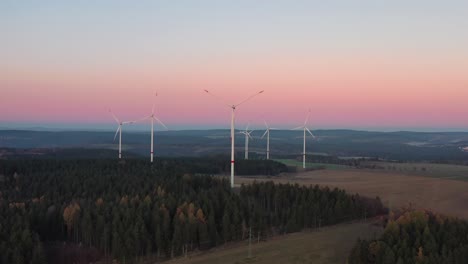 Luftaufnahme-Von-Windkraftanlagen-Mit-Rotierenden-Rotorblättern-In-Ländlicher-Landschaft-Nach-Sonnenuntergang
