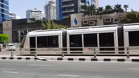 Metro-subway-train-moving-across-the-city-streets-from-left-to-right-in-the-middle-of-the-hot-day-in-Jumeirah-Beach-Residence-alone-side-street-vehicles-slow-pan-b-roll-clip