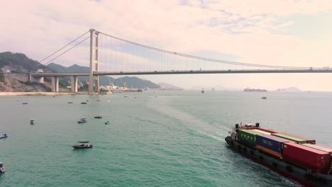 Small-Feeder-class-Container-ship-in-Hong-Kong-bay-with-Tsing-Ma-bridge-in-the-background,-Aerial-view