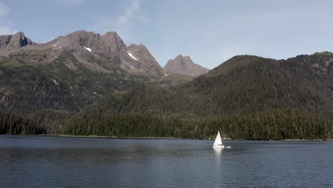 Solitary-Sailboat-Sailing-In-Sea-with-Scenic-View-Of-Mountains-And-Forest-In-Alaska-USA---panning-wide-shot