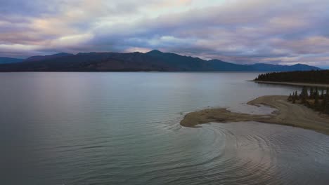 Kluane-Lake-at-dramatic-sunset-behind-mountains,-aerial-drone-shot