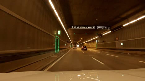 Car-drive-through-an-illuminated-tunnel,-following-another-car-and-coming-out-of-the-underground-at-the-end-of-the-4k-clip---Mittlerer-Ring-of-Munichm-bavaria