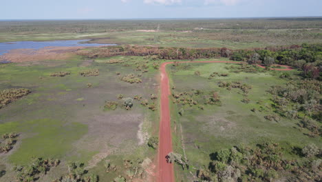 High-Aerial-Slow-Moving-drone-shot-of-Long-Straight-Red-Road-and-Green-Bushland-near-Holmes-Jungle-Nature-Park,-Darwin,-Northern-Territory