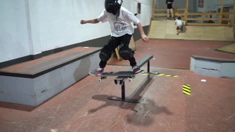 Young-skateboarder-with-mask-jumping-on-rail-and-grinding-during-indoor-skateboard-training
