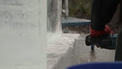 Ice-chips-flying-as-scultor-uses-saw-on-ice-block,-Slow-Motion