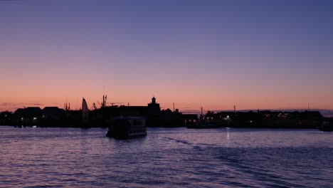 Stationäre-Aufnahme-Von-Silhouetten-Vorbeifahrender-Vergnügungsboote-Bei-Sonnenuntergang-Zur-Blauen-Stunde-In-Einem-Wunderschönen-Hafen