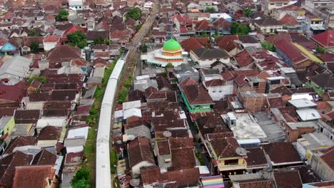 Passenger-train-passing-residential-area-of-Malang-City,-Java,-Indonesia,-aerial