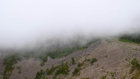 Wide-shot-of-fast-cloudscapes-covering-hiking-trails-in-rural-landscape-on-top-of-mountain