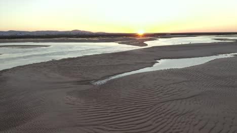 Die-Sonne-Brennt-Bei-Sonnenuntergang-Auf-Dem-Horzion,-Während-Die-Drohne-Rückwärts-Fliegt-Und-Den-Wunderschönen-Goldenen-Strand-Freigibt