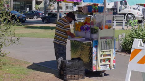 Fruit-stand-worker-peeling-fruit-in-Palisades-park,-Santa-Monica,-California