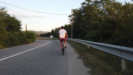 Ein-Junge-Fährt-An-Einem-Sommertag-Bei-Sonnenuntergang-Mit-Dem-Fahrrad-Auf-Einer-Landstraße