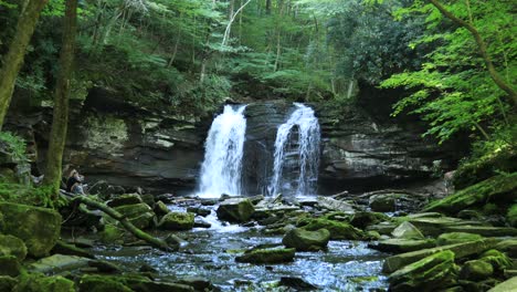 A-young-woman-sits-beside-Seneca-Falls,-a-large-waterfall-located-along-Seneca-Creek,-within-the-Spruce-Knob-Seneca-Rocks-National-Recreation-Area-in-West-Virginia