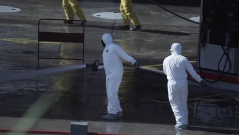 A-group-of-men-in-biohazard-suits-clean-the-floor-of-a-gas-station-with-a-water-stream-coming-from-a-firefighter-hose-during-COVID-19-pandemic