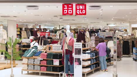 Compradores-Femeninas,-Mujeres,-Buscan-Y-Compran-Ropa-De-Moda-En-El-Logotipo-Y-La-Tienda-De-La-Marca-De-Ropa-Japonesa-Uniqlo-En-Hong-Kong