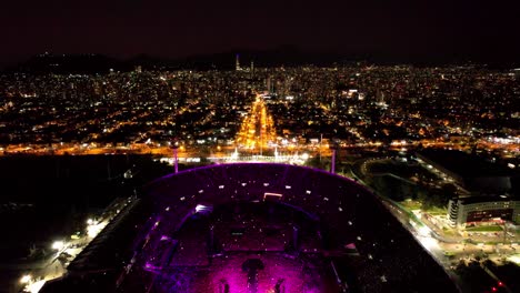 Hochhaus-Aus-Der-Luft,-Das-Die-Skyline-Von-Santiago-Bei-Nacht-Mit-Der-Coldplay-Liveshow-Im-Nationalstadion-Freigibt