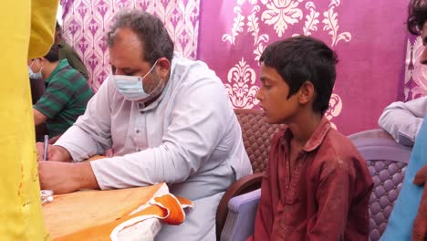 A-doctor-wearing-face-mask-and-talking-to-the-child-about-his-ailment-in-the-flood-relief-camp-installed-in-Sindh,-Pakistan