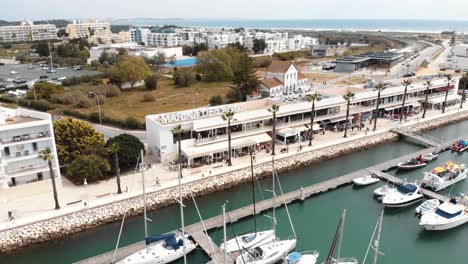 Marina-de-Lagos-center-in-Lagos-bay-with-anchored-boats-in-Faro,-Algarve,-Portugal--Low-angle-Aerial-Orbit