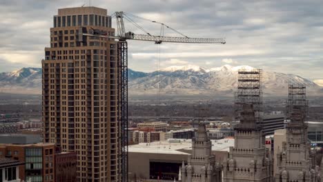 Downtown-Salt-Lake-City,-Utah-time-lapse-with-a-crane-moving-in-the-foreground,-the-Mormon-Temple-and-mountains-and-a-cloudscape-in-the-background