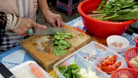 Old-Hands-Chopping-Pak-Choi-at-Open-Air-Kitchen,-Additional-Vegetables-on-Table---Medium-Shot,-25p
