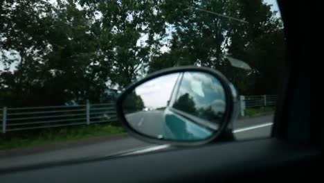 Looking-at-the-reflection-in-the-car-rear-mirror-while-driving-on-road