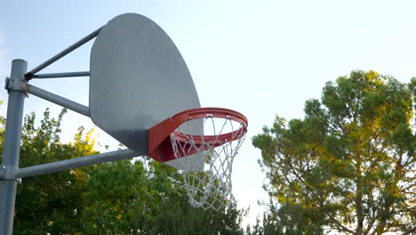 A-basketball-hoop-with-metal-backboard,-orange-rim-and-a-net-in-a-park-court-at-sunrise