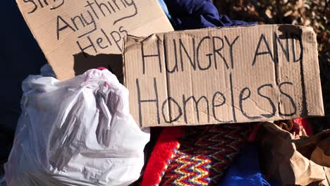 Cardboard-signs-that-read-"Single-Mom,-Anything-Helps"-and-"Hungry-and-Homeless"-sitting-on-pile-of-stuff