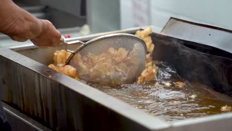 Slow-motion-of-using-strainer-to-lift-hot-curly,-tornado-fries-out-of-hot-oil