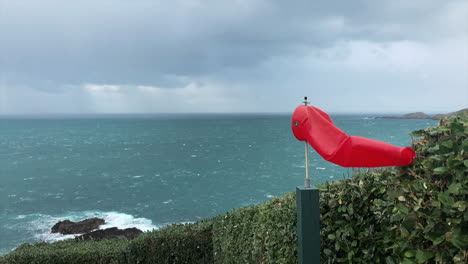 Slow-Motion,-Small-windsock-blows-at-a-the-edge-of-a-helipad,-rain-in-the-background-falling-onto-the-sea